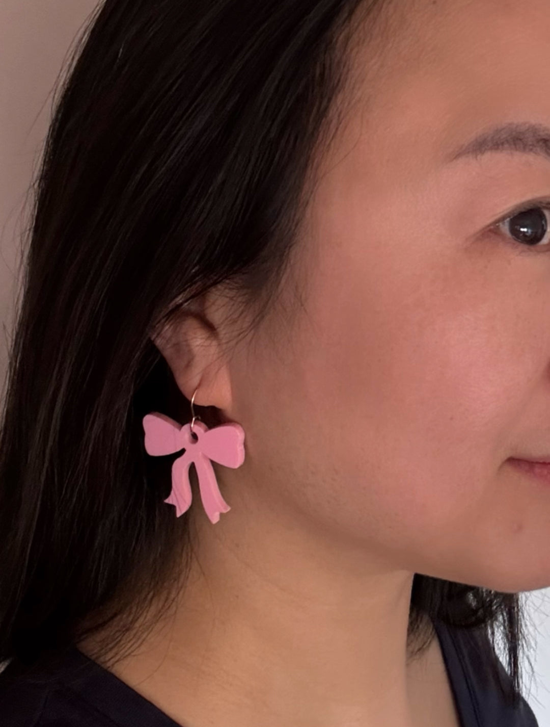 Person wearing pink bow-shaped earrings with a neutral background