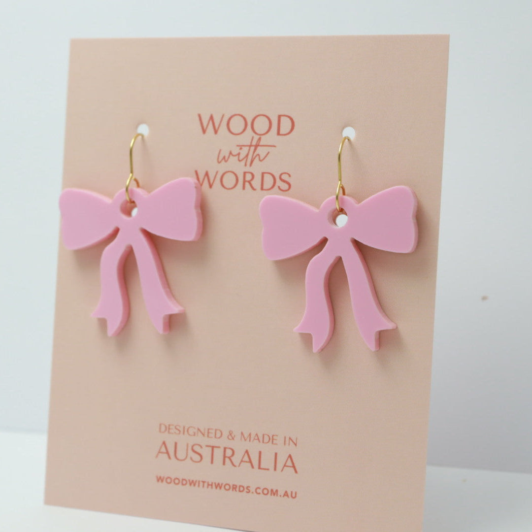 Pink bow earrings on a 'Wood with Words' branded card